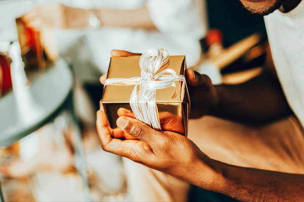 Person holding a gold gift box with a white ribbon in an indoor setting